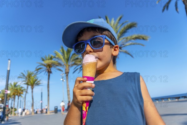 Young boy wearing sunglasses and cap enjoying a refreshing ice cream cone on a sunny summer day at
