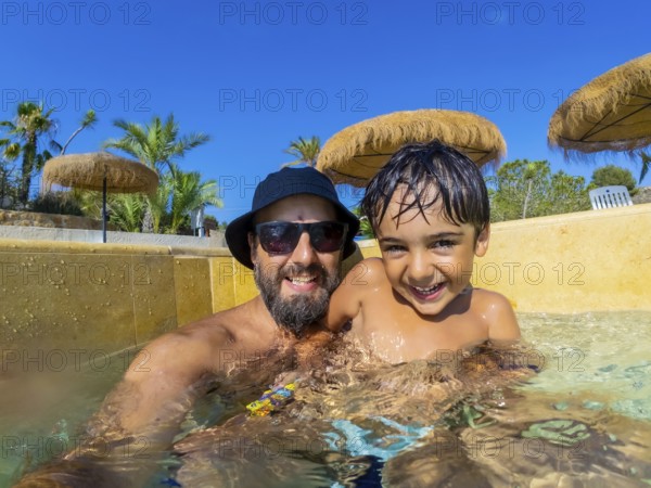 Happy father and son are spending quality time together, playing in swimming pool during summer