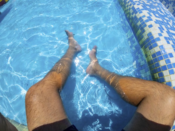 Point of view shot capturing a man relaxing in a swimming pool, legs submerged in the refreshing