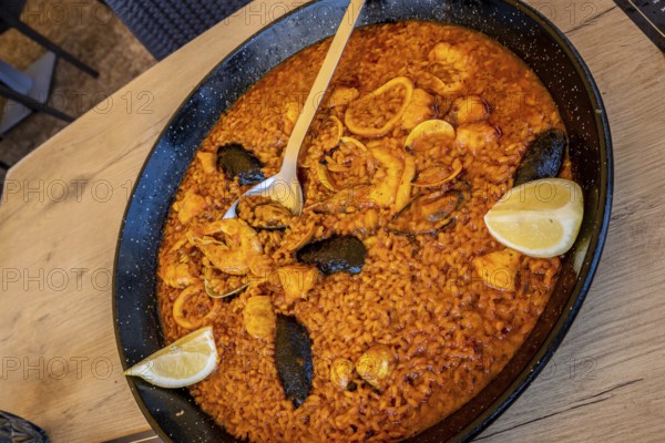 Large pan of delicious seafood paella with shrimps, mussels, squid, clams, and lemon wedges, ready