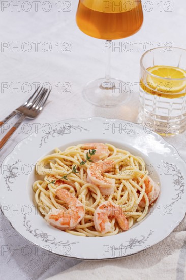 Pasta with shrimp and thyme, served on a white plate, with a glass of white wine, the table is set,