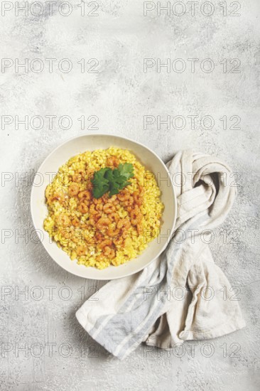 Risotto with shrimp, in a bowl, on a textured surface, with a side dish of fresh coriander,