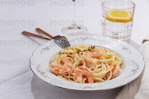 Pasta with shrimp and thyme, served on a white plate, with a glass of white wine, the table is set,
