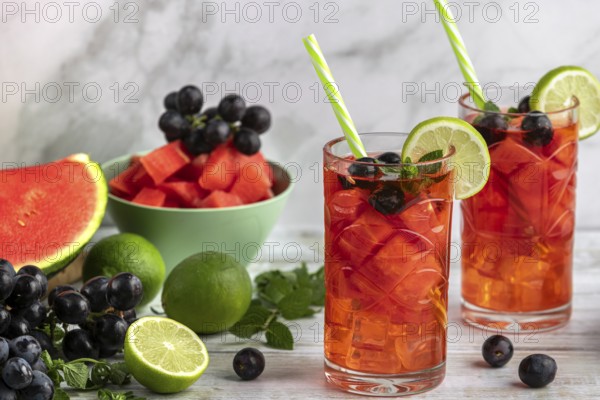 Two glasses of watermelon, grape and lime drink surrounded by ingredients