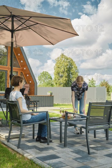 A young woman brought plates to the patio table to lay out grilled food on backyard