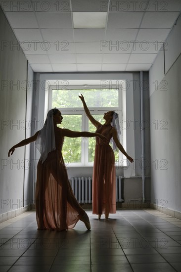 Silhouette of two dancers performing graceful artistic moves with their hands in corridor of