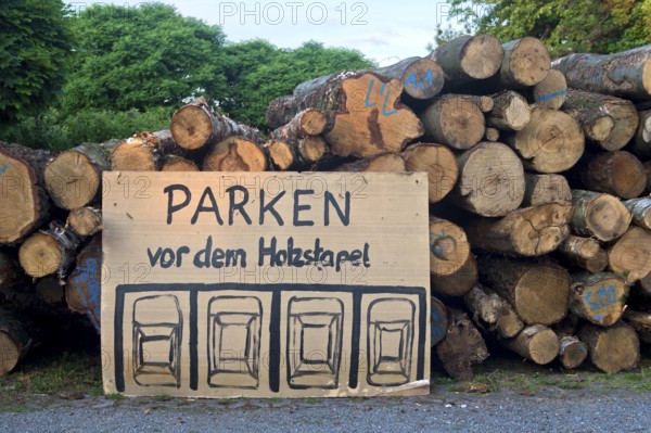 Parking regulations for cars, handwritten and hand-drawn parking sign in front of a woodpile,