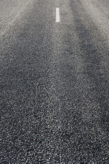 Rustige asfaltweg zonder voertuigen, met een enkele witte middenlijn zichtbaar. De weg strekt zich