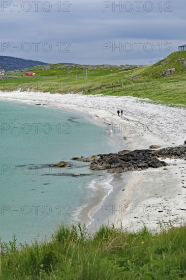 Coastal landscape with grassy areas, calm sea and walkers on a white sandy beach, Eriksay, Isle of