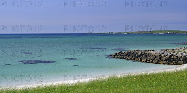 Clear blue sky over a rocky coastline with green grass and blue water, Outer Hebrides, South Uist,