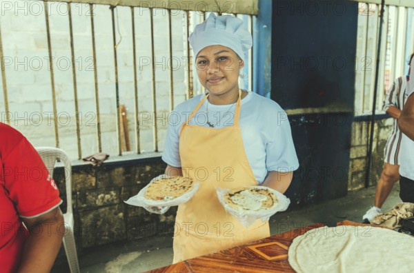 Portrait of a vendor serving and holding two pupusas. Smiling female vendor holding two plates of