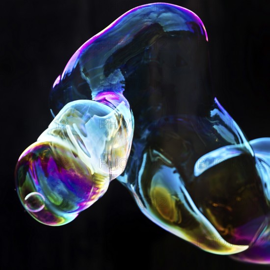 Large, iridescent soap bubble tube in the colours of the rainbow against a black background,