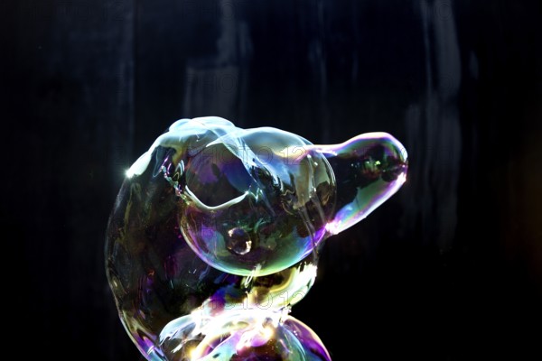 A shimmering and floating soap bubble in the colours of the rainbow against a black background,