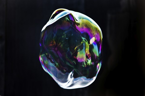 A large iridescent and floating soap bubble in the colours of the rainbow against a black
