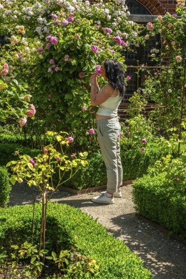 Full-length young woman smelling roses in Ystad monastery garden, SkÃ¥ne County, Sweden,