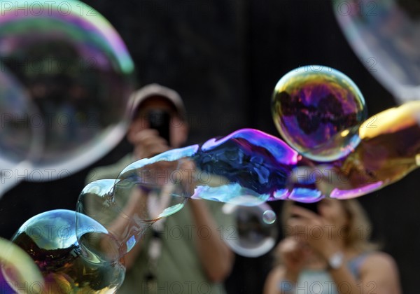 A man and a woman photograph iridescent soap bubbles in front of a black background,