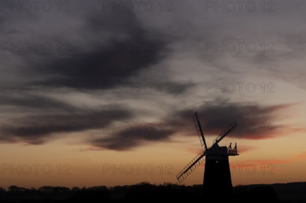 Windmill silhouette at sunset with a red sky and dark clouds, Burnham Ovary Staithe, Norfolk,