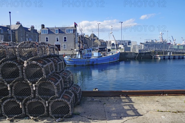 A harbour with fishing boats and stacked nets under a clear sky, Fraserburgh Aberdeenshire,