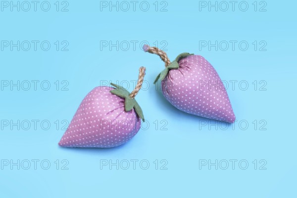 Two handmade pink fabric strawberries on blue background as creative DIY decoration