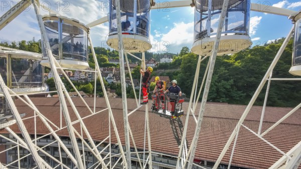 Workers in a Ferris wheel with lifting platform, surrounded by green hills and blue sky, fire