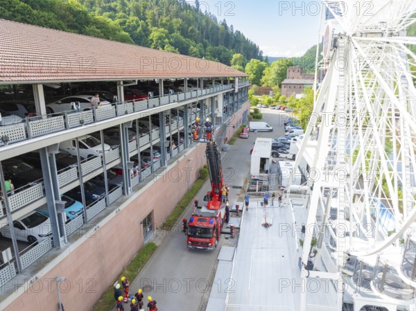 Ferris wheel near a multi-storey car park, fire engines and people in sunny weather, fire brigade