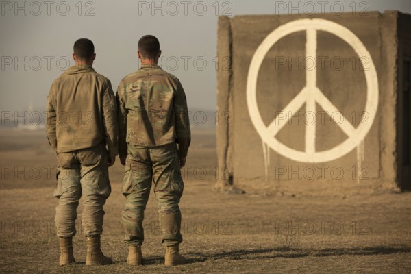 Two soldiers facing painted peace symbol on brick wall. Contrast between duty and hope in times of