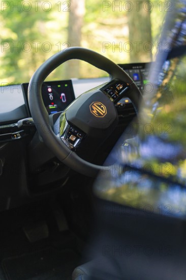 Interior of a car with focus on the steering wheel and digital displays, background of trees, MG 4,