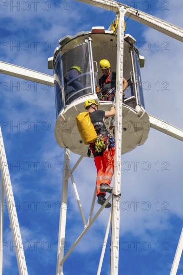 Two workers in safety equipment during maintenance work on a Ferris wheel in a cabin, fire brigade