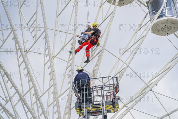 Firefighters rescue person by abseiling from Ferris wheel, fire brigade exercise for gondola