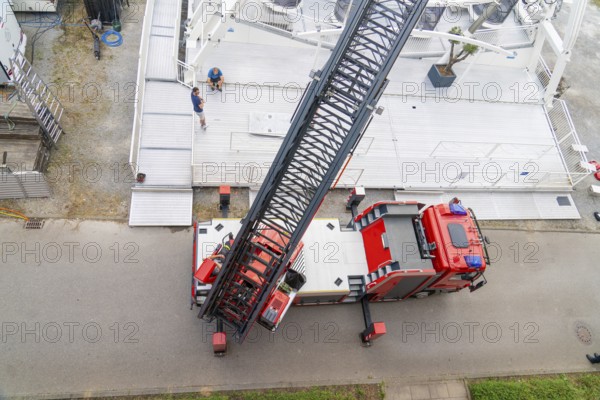 A large fire engine with crane boom is parked on a road, fire brigade exercise for gondola rescue,