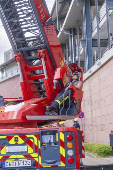 Firefighter resting on an extended lifting platform next to a building, fire brigade exercise for