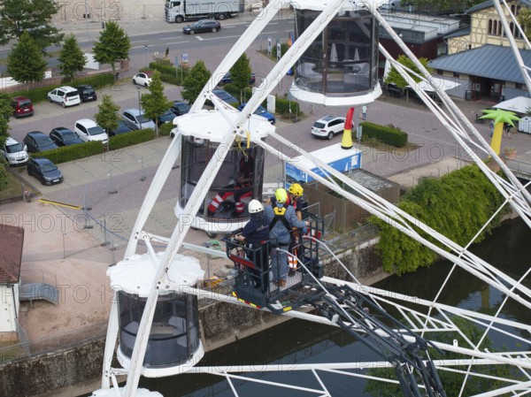 Firefighters during a rescue exercise on a Ferris wheel in an urban environment with parked cars,