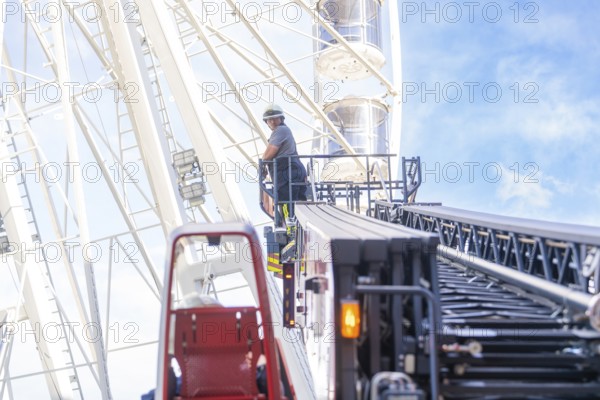 Firefighter on a lifting platform next to a Ferris wheel in front of a clear sky, fire brigade