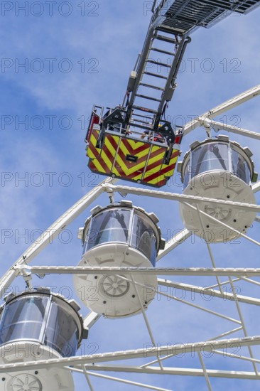 Rescue ladder of the fire engine reaches the cabins of the Ferris wheel, background with blue sky,