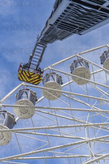 Fire brigade ladder reaches up to the Ferris wheel, ready for an operation in the clear sky, fire