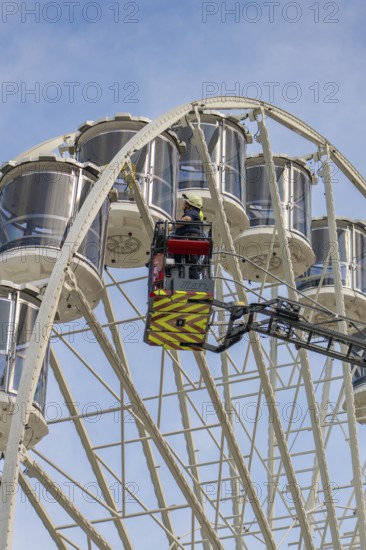 Fireman in the rescue cage is lifted to the cabins of the Ferris wheel, blue sky as background,