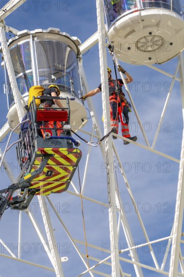 Rescue workers on a Ferris wheel during safety work under blue sky, fire brigade exercise for