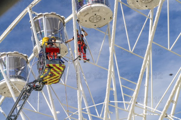 Firefighters at work on a high Ferris wheel under a blue sky, Fire brigade exercise for gondola