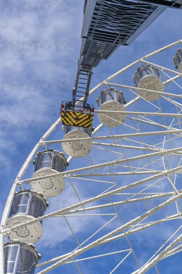 Fire brigade ladder extends against the sky to the cabins of the Ferris wheel, ready for a rescue,