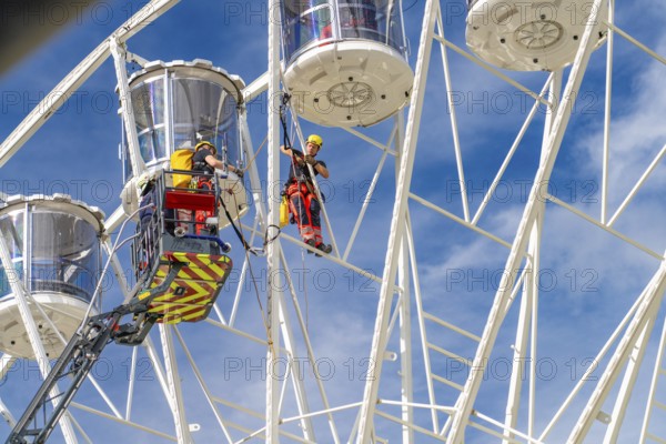Workers secured on a Ferris wheel during rescue work under blue sky, fire brigade exercise for