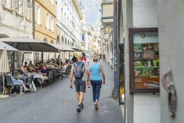 Couple walking through a pedestrian zone with restaurants in the background, mountain view in