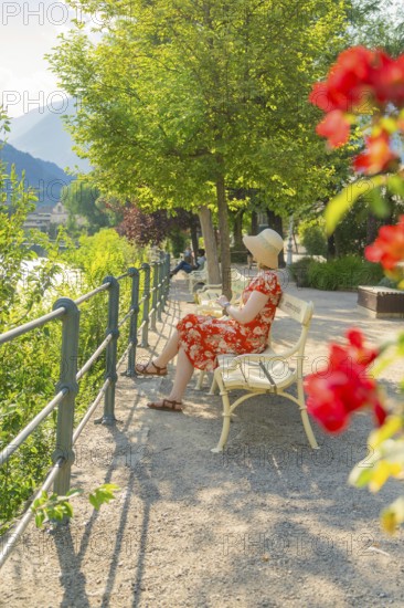 Woman in summer dress sitting on park bench, surrounded by flowers in relaxed atmosphere, Merano,