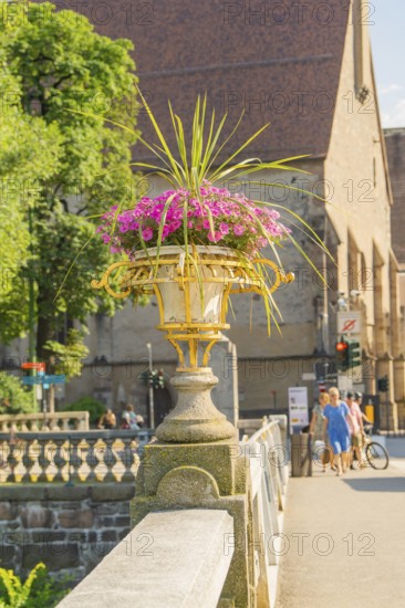 Stone bridge with flower pot, church and pedestrians in the background, Merano, South Tyrol, Italy