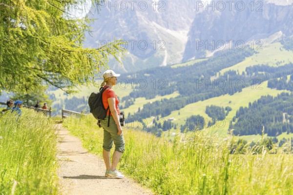 Woman standing on a path and enjoying the wide view of the green mountains, Alpe di Siusi,