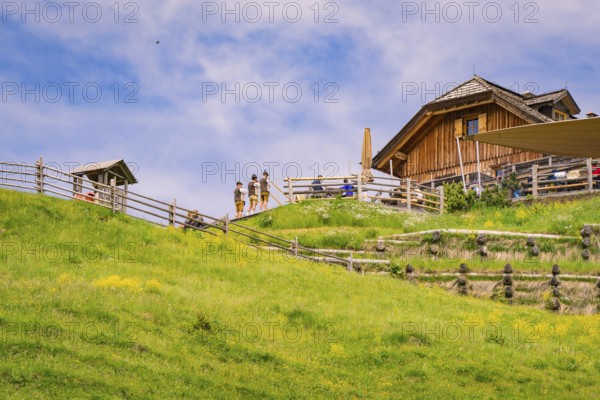 A wooden hut stands on a grassy slope, surrounded by traditional wooden structures, Zallinger Alm,