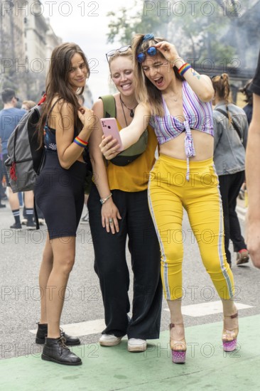 Three cheerful young women wearing rainbow bracelets are taking a selfie with a smartphone during a