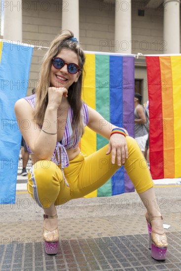 Young woman crouching and smiling brightly, wearing stylish sunglasses and vibrant, colorful