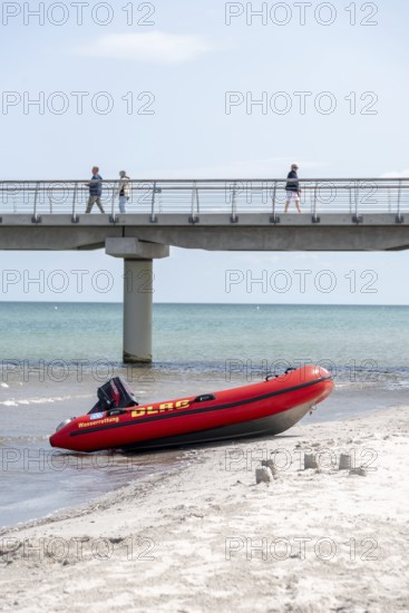 A DLRG lifeboat lies on the beach in front of a bridge with walkers and the sea in the background,