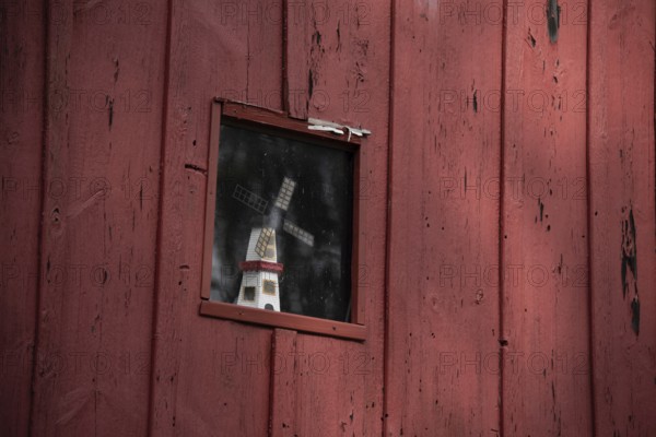 A small window in a red wooden faÃ§ade with a windmill as decoration behind it, Prerow,