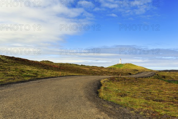 Winding tarmac road leads through barren volcanic landscape, Reykjanesviti lighthouse on the